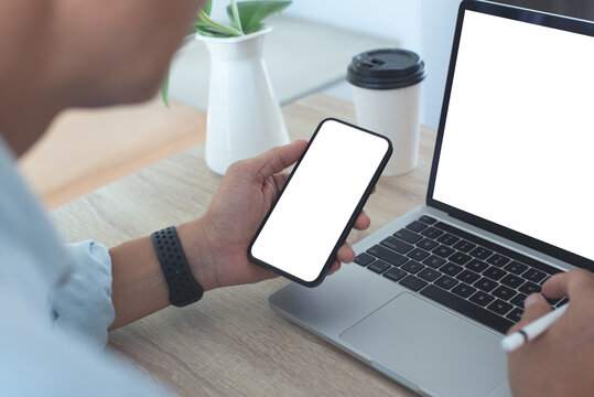 Mockup Image Of Mobile Phone, Business Man Hand Holding Blank Black Screen Mobile Phone During Working On Laptop Computer At Home Office