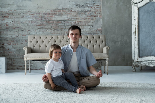 Young father trying to meditate sitting in lotus yoga pose with little son kid