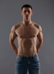 Fit and muscular. Shirtless guy in jeans grey background. Sporting man with fit torso © Olena