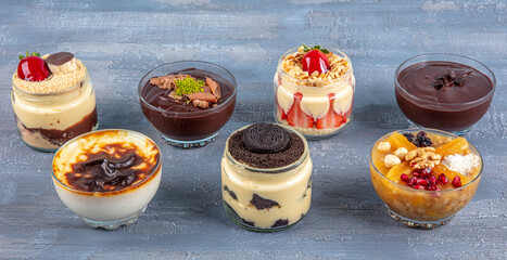 Milky desserts. Various milky fruit desserts decorated with mint and chocolate in glass cups on the light marble background. Taste and pleasure. Sweet life. Pleasant moments.