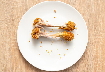 Two chicken bones as left over on white plate. Unhealthy fast food, chicken legs, top view