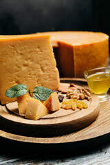 Close up of cheddar cheese piece on wooden brown board with honey, nuts and raisins. Perfect wine snack