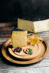Organic gouda cheese piece demonstration, cheese, honey, raisins and nuts on wooden brown board