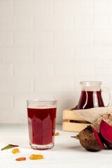 A glass of beet kvass, pieces of beetroot and a jug with a drink on a light background. Vertical,...