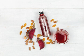 Beet kvass in a bottle and in a cup on a light wooden background, top view.