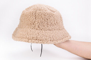 A hand holds a female panama made of faux fur on a white background. Beige artificial fur. Beige short pile faux fur.