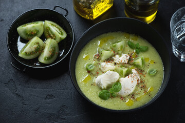 Bowl of green tomato gazpacho soup served with mozzarella, elevated view on a black stone surface, studio shot