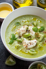 Gazpacho soup made of green tomatoes and served with mozzarella cheese in a white bowl, vertical shot, close-up