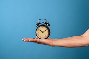 Wake up and get up, it's time to act, concept. Clock and alarm clock, attention it's time to do. A man's hand holds a vintage alarm clock, a photo on a blue background