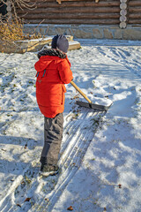 Fototapeta na wymiar A boy shovels snow in the backyard of the house
