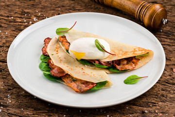 Gourmet crepes with poached egg, grilled bacon, cheese and herbs for breakfast