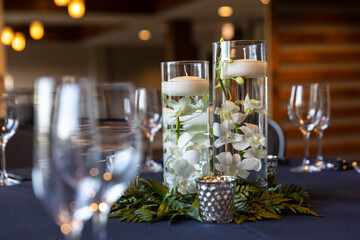 A centerpiece at a wedding with wine glasses on the table, flowers and floating candles in pillar...
