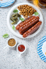 White takeaway plate with bbq german bratwurst, mini pretzels and pickles, flatlay on a beige granite background, studio shot