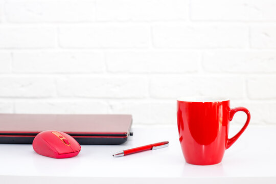 Office work space with red laptop, computer mouse, pen and smiling cup of coffee.