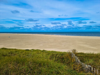 Fototapeta na wymiar Panorama view of Dunes with marram gras and an empty beach on the Dutch island of Texel on a with a blue cloudy sky in summer. Tourism and vacations concept. National park Duinen van Texel