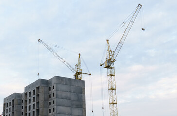 Fototapeta premium Against the background of the sky, there is a multi-storey building under construction and two cranes