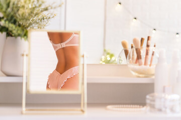 Reflection in table mirror of woman body in underwear. Female party preparation. Сhristmas, light...