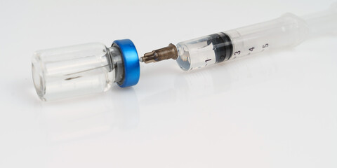 A syringe and a jar of injection lie on a white reflective surface.