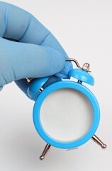 On a white background in a hand with a blue glove an alarm clock with a white surface.