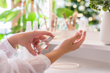 Woman applying perfume on her hand sitting near dressing table with make up accessories and table...