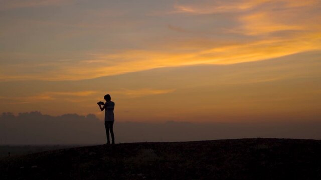 Silhouette of an Indian photographer taking photos with his camera during the sunset. Man taking pictures with his camera during the sunset. Photographer takes out his camera and takes photo.	