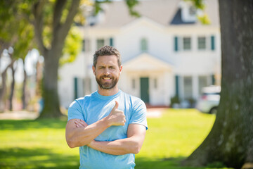 happy bearded man standing showing thumb upon house background, broker