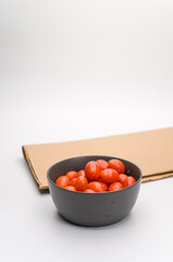 datterini tomatoes in a dark stoneware bowl and food paper on a white background