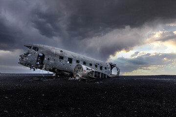 Transport flight time on Iceland beach. Old plane wreck on black sand. Silver colored old airplane without engines on the ground in the evening with dramatic clouds at sunset