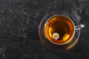 Healthy chamomile tea in a glass teacup on black stone background copy space