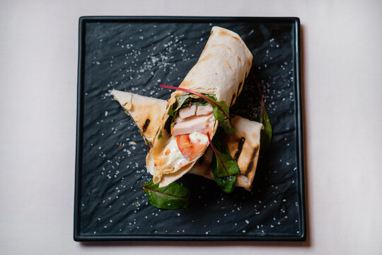 Fototapeta Sliced kebab with ham, herbs, tomato and sauce on black stone plate. Food cooking process. Shawarma take away street food.