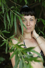 Young European woman under the green willow tree leaves. Bikini style.