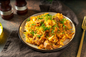 Braised cabbage. Stewed cabbage or bigos with turkey meat in a ceramic plate on a dark background. Traditional Polish dish	