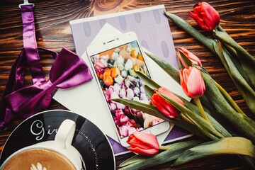 Cup of coffee, phone and tulips flowers on wooden brown background in spring