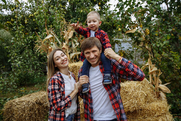 family with a little son in red shirts on a background of hay and pumpkins