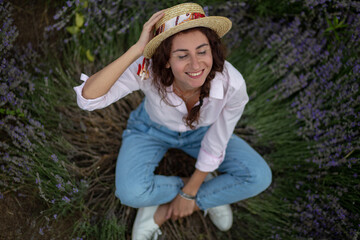 smiling beautiful woman in straw hat sitting on the lavender field