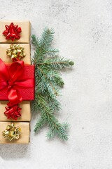 Many small gift boxes with a large red box in the center, wrapped in holiday paper with fir branches on gray background. Gifts for Christmas and New Year. Festive concept, top view.
