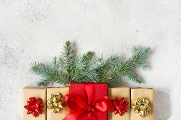 Many small gift boxes with a large red box in the center, wrapped in holiday paper with fir branches on gray background. Gifts for Christmas and New Year. Festive concept, top view.