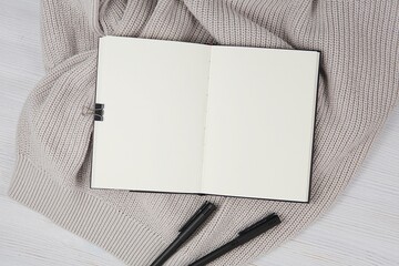 Open blank notebook top view, planner, journal, diary mockup for text or design, flat lay with cozy sweater and gel pens.