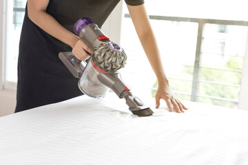 Woman disinfecting mattress with vacuum cleaner, closeup.