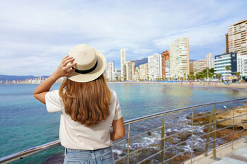 Young woman holds hat on promenade in front of the skyline from Benidorm Downtown, Spain