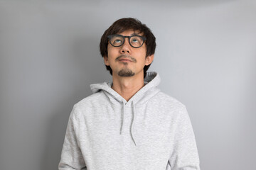 Adult asian man in grey sweater and eyeglasses smiling on a grey background.