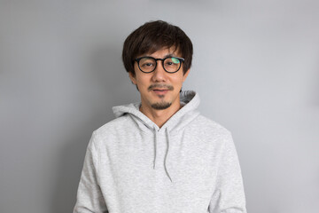 Adult asian man in grey sweater and eyeglasses smiling on a grey background.
