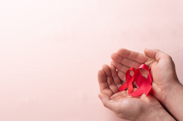healthcare and medicine concept two hands holding red ribbons HIV and AIDS awareness on brown background close up