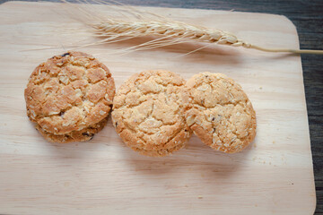 Three delicious oatmeal cookies with spikelets on wooden cutting board on table.