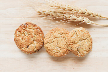 Three delicious oatmeal cookies with spikelets on wooden cutting board on table.