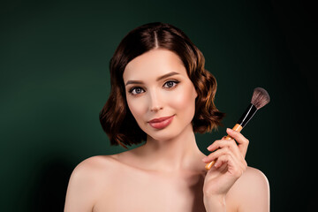 Portrait of smiling cool professional makeup artist girl with naked shoulders hold big brush isolated on green color background