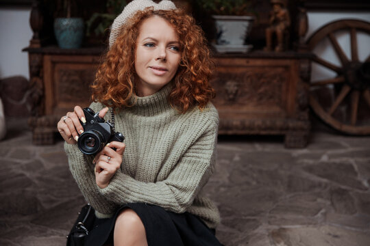 A woman in a beret and a green sweater holds a camera in her hands and takes shoots