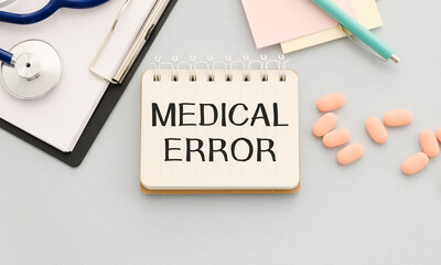 MEDICAL ERROR written on a light wooden table near a stethoscope and pills. Medical concept