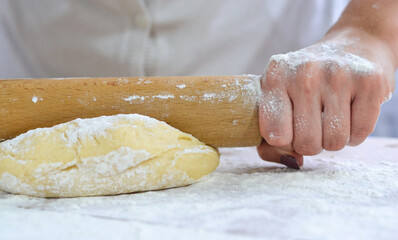 A woman is kneading the dough with a rolling pin on a wooden kitchen table