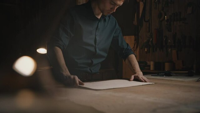 Tracking shot of professional tailor working with pattern and fabric at his workshop, painting with pencil